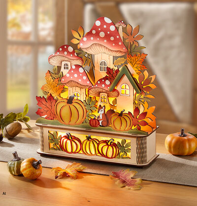 Beleuchtetes Herbstdeko-Haus mit Fliegenpilzen, K&uuml;rbissen und bunten Herbstbl&auml;ttern auf einem Holztisch